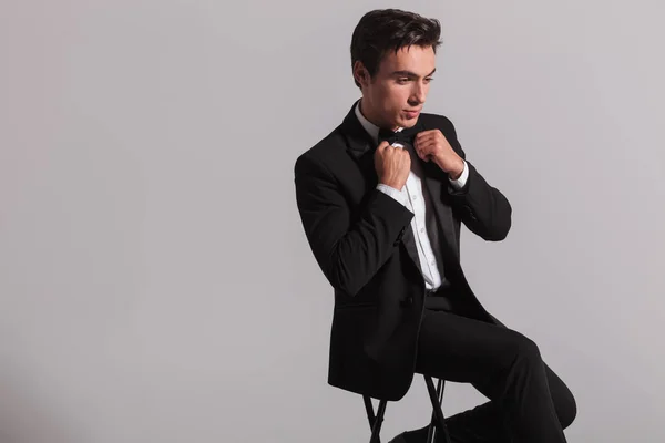 Side view of an elegant young man fixing his bowtie — Stock Photo, Image