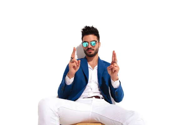 Joven elegante hombre sentado y sosteniendo los dedos cruzados — Foto de Stock