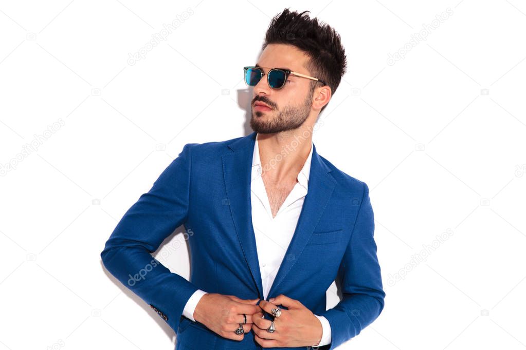 elegant man wearing sunglasses buttoning his suit and looks away