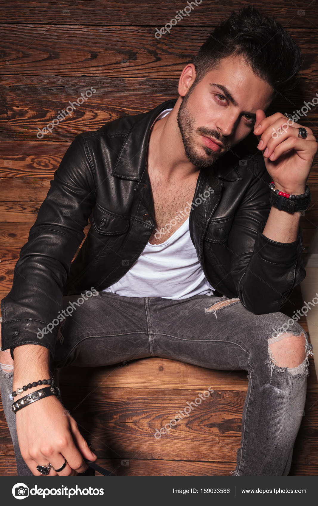 Hombre en chaqueta de cuero y jeans sentado sobre fondo de madera Foto de stock 159033586 feedough