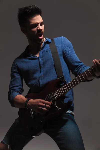 Молодой гитарист кричит, играя на своей электрогитаре — стоковое фото