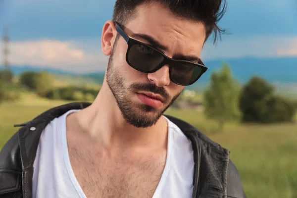 Hombre joven en chaqueta de cuero y gafas de sol posando al aire libre —  Fotos de Stock