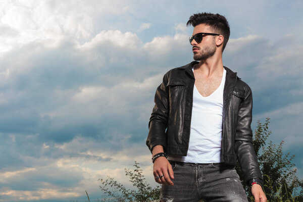 young sexy man in leather jacket and sunglasses standing outdoor