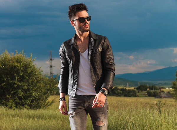 young fashion man in leather jacket and sunglasses walking 