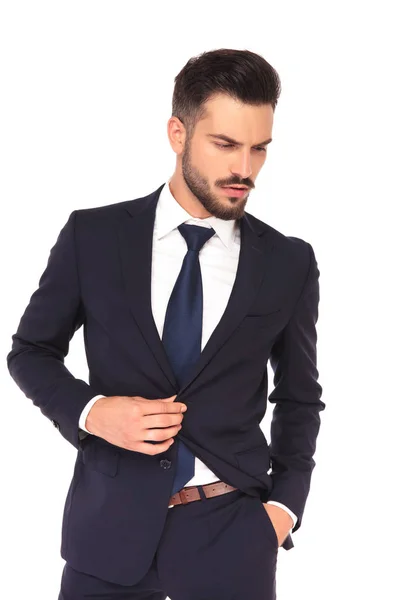 Joven hombre de negocios sosteniendo botón de traje mira hacia abajo —  Fotos de Stock