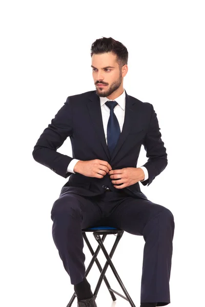 Hombre de negocios cerrando su traje y mira a un lado mientras está sentado —  Fotos de Stock