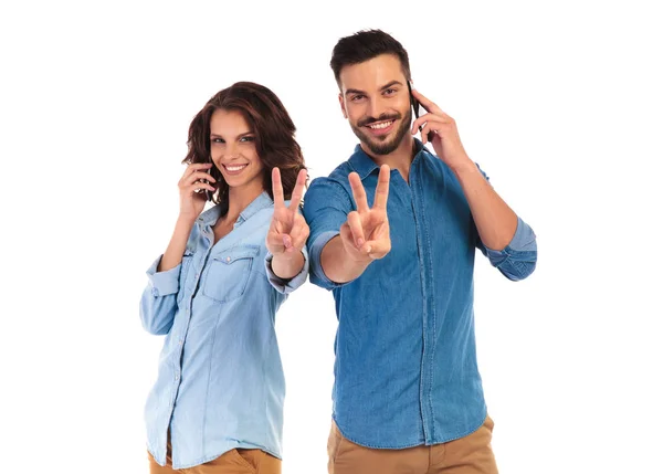 Випадкова пара, що говорить на своїх телефонах, робить знак перемоги — стокове фото