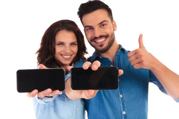 Happy casual couple showing phones and man makes ok sign — Stock Photo, Image