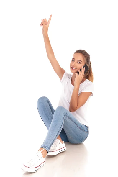 Sorrindo mulher casual aponta para cima e fala em seu telefone — Fotografia de Stock