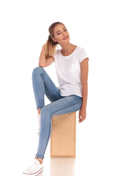 Sonriente mujer jugando con su cola de caballo sentado en caja de madera — Foto de Stock