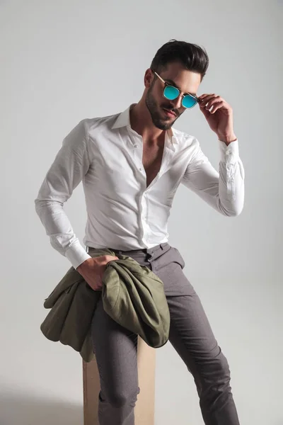 Sexy giovane uomo tenendo cappotto e togliersi gli occhiali da sole — Foto Stock