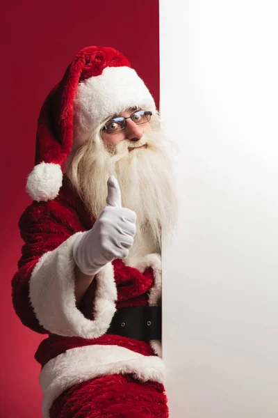 Kerstman zitten in de buurt van leeg bord en maakt ok teken — Stockfoto
