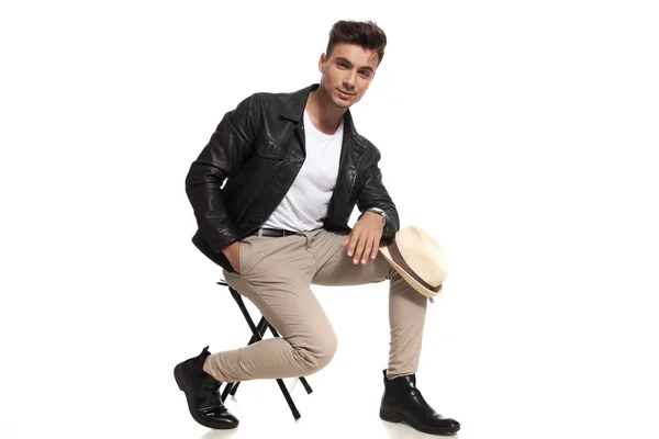 Casual jongeman zit op stoel met hoed op knie — Stockfoto