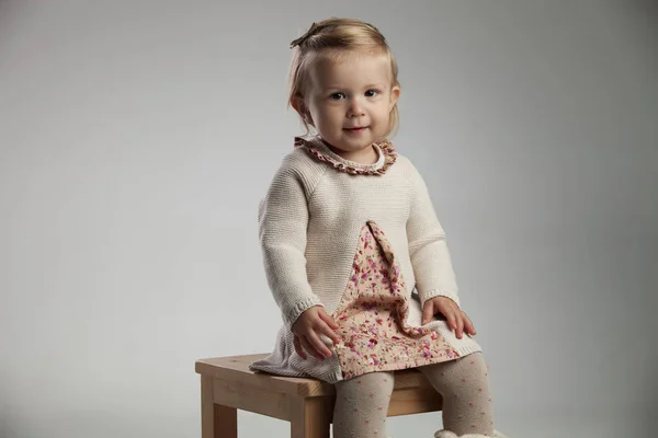 Pequena menina feliz está sentada em uma cadeira — Fotografia de Stock