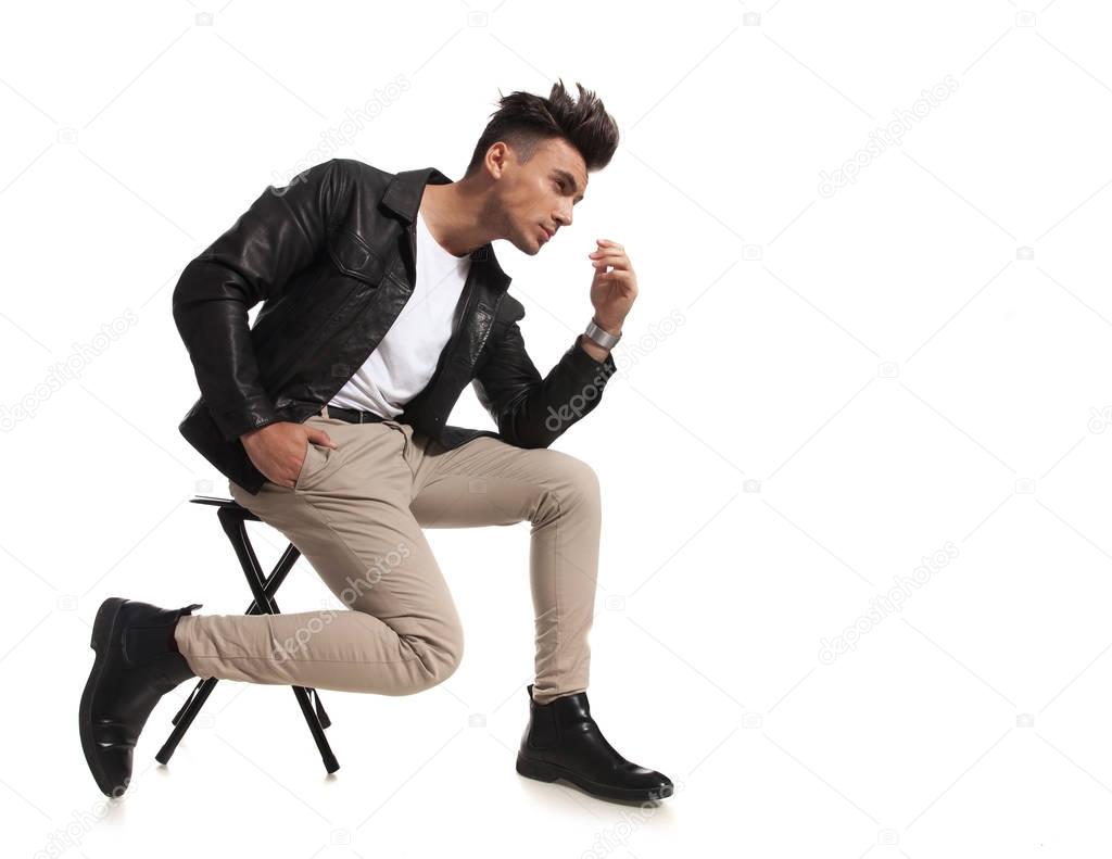 side  of a pensive fashion man sitting on a chair