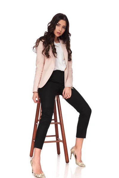 Young fashion woman posing seated on a stool in studio — Stock Photo, Image