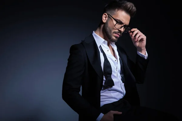 Sitter elegant man i smoking och ogjort bowtie fastställande glasögon — Stockfoto