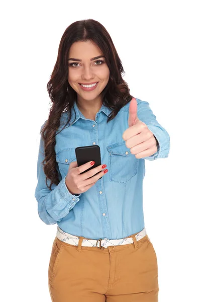Mujer casual joven hace el signo de ok mientras sostiene el teléfono — Foto de Stock