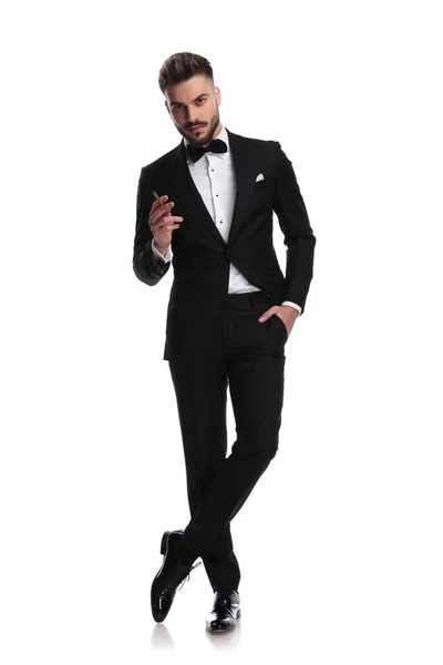 Smiling young elegant man in tuxedo is smoking — Stock Photo, Image