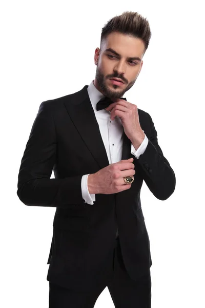 Elegnat man in tuxedo is fixing his bowtie — Stock Photo, Image