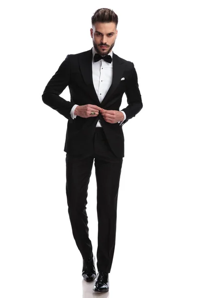 Serious fashion model buttoning his tuxedo while walking — Stock Photo, Image