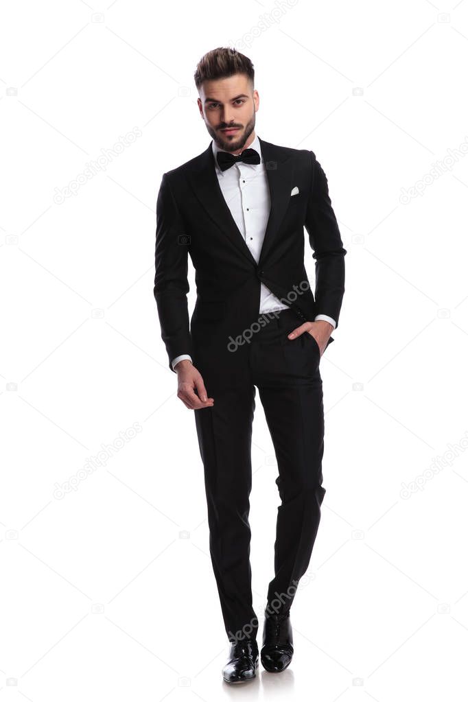 smiling man in tuxedo stands with one hand in pocket