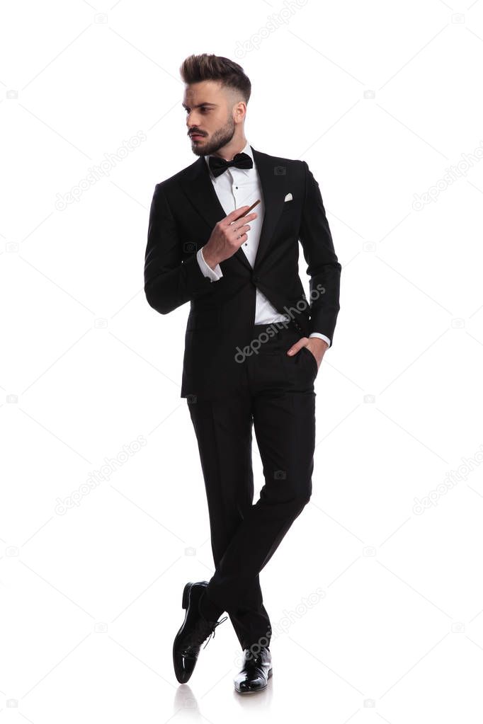 cool man in tuxedo is smoking and looks to side