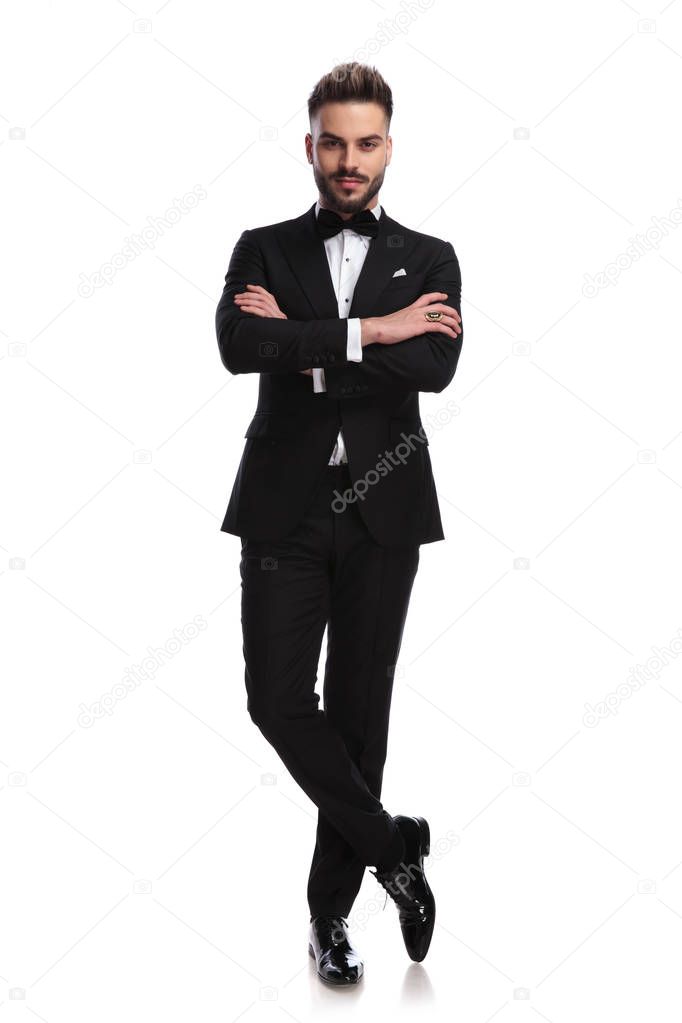 happy sexy young man in tuxedo standing with hands crossed
