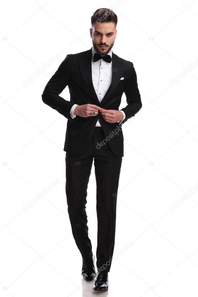 serious fashion model buttoning his tuxedo while walking