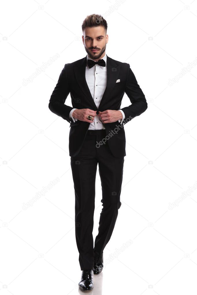 smiling elegant man in tuxedo buttoning coat while walking 