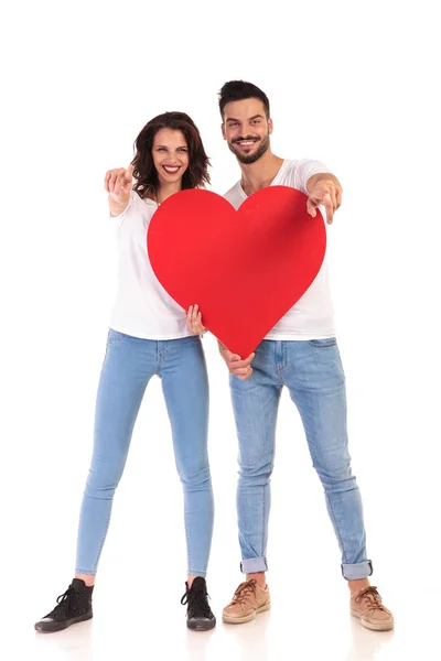 Jovem casal casual segurando um grande coração e aponta dedos — Fotografia de Stock