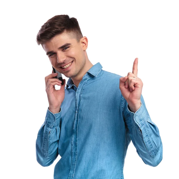 Lächelnder junger Mann, der lässig am Telefon spricht, zeigt nach oben — Stockfoto