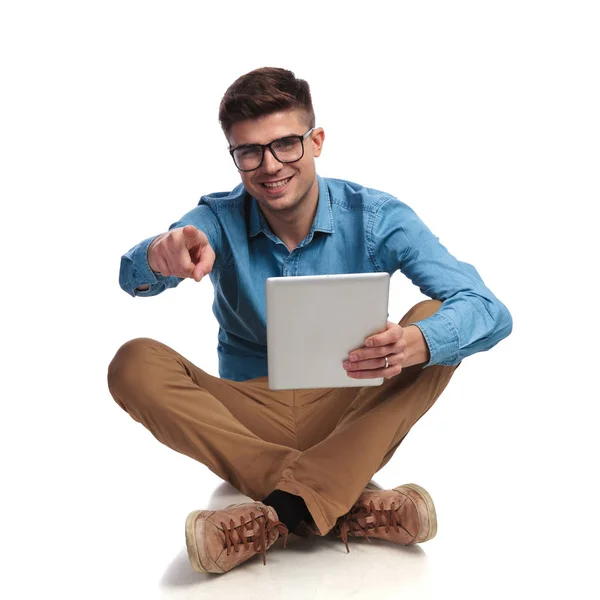 Young man reading on tablet and points finger while sitting — Stock Photo, Image