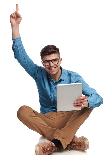 Hombre apuntando con el dedo hacia arriba mientras sostiene la tableta y se sienta —  Fotos de Stock