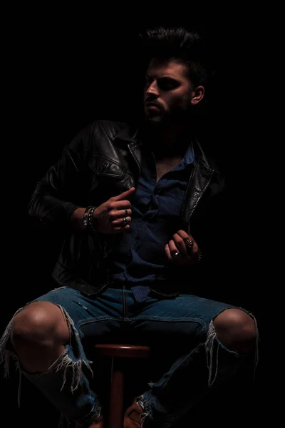 Fashion man sitting looks to side while holding jacket collar — Stock Photo, Image