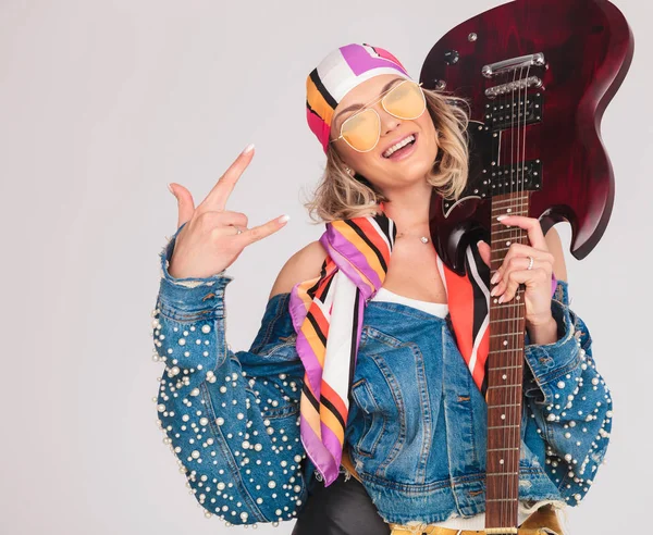 Mujer hace rock en signo mientras sostiene la guitarra en el hombro —  Fotos de Stock