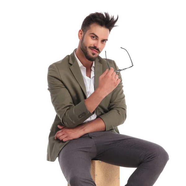 Retrato de sonriente hombre elegante sosteniendo gafas mientras está sentado — Foto de Stock