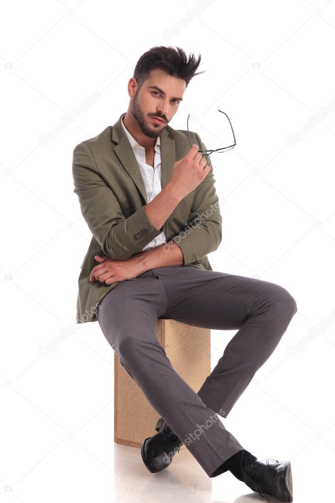 stylish young man sitting on wooden box while holding glasses
