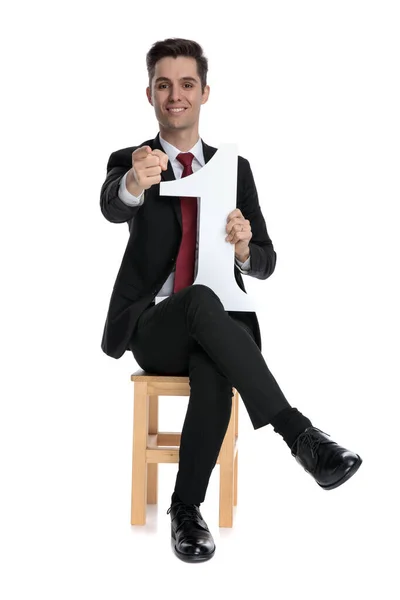 Hombre de negocios guapo señalando hacia adelante y sosteniendo un número uno —  Fotos de Stock