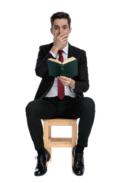 Förbluffad affärsman täcker sin mun och håller i en bok — Stockfoto