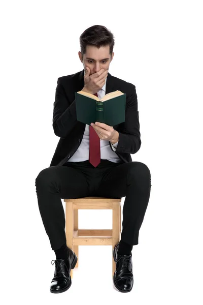 Hombre de negocios asombrado cubriéndose la boca y leyendo un libro — Foto de Stock