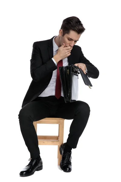 Homem de negócios incrível cobrindo sua boca e olhando em sua briefca — Fotografia de Stock