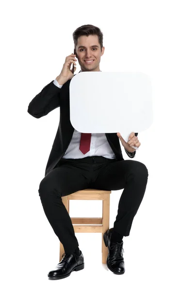 Empresário falando em seu telefone e segurando uma bolha de discurso — Fotografia de Stock