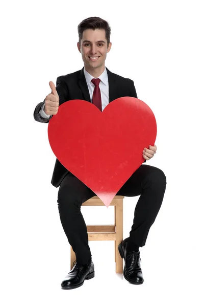 Homme d'affaires joyeux tenant une forme de coeur et donnant pouces vers le haut — Photo