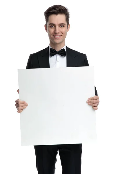 Feliz hombre elegante en esmoquin sonriendo y sosteniendo tablero vacío — Foto de Stock