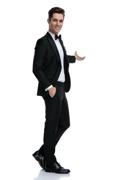 Smiling young groom in tuxedo presenting to side — Stock Photo, Image