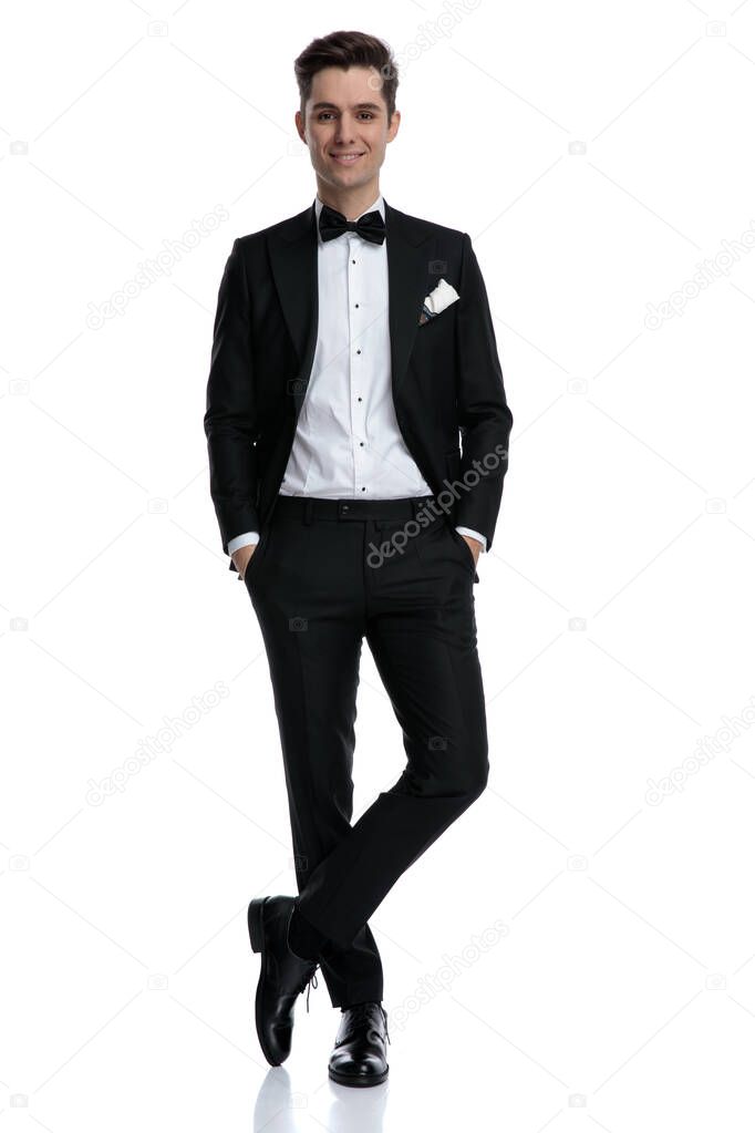 young elegant man in tuxedo smiling and holding hands in pockets
