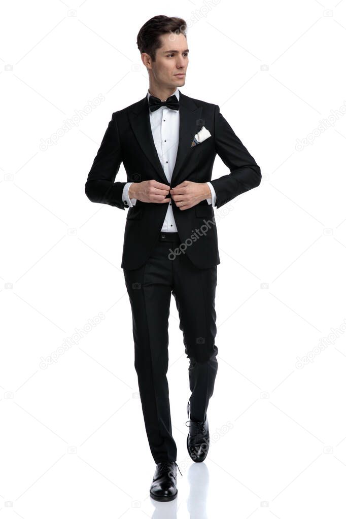 elegant young groom arranging coat and walking
