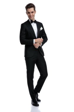 Smokinli mutlu damat gömleğini düzeltiyor ve gülümsüyor.