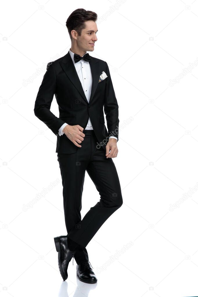 smiling groom in tuxedo looking to side on white background